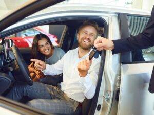 Happy couple receiving car keys from a dealership representative while sitting in a new car.
