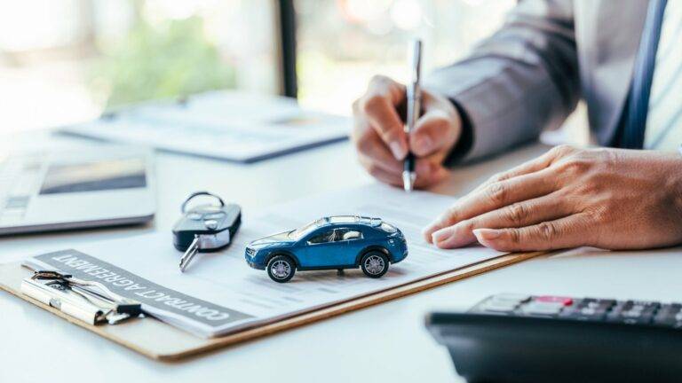 Businessperson signing a vehicle finance agreement with a blue toy car and car keys on the document.