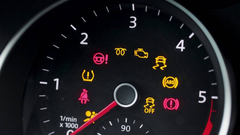 Car dashboard with various warning lights illuminated, including ABS, engine, and seatbelt indicators