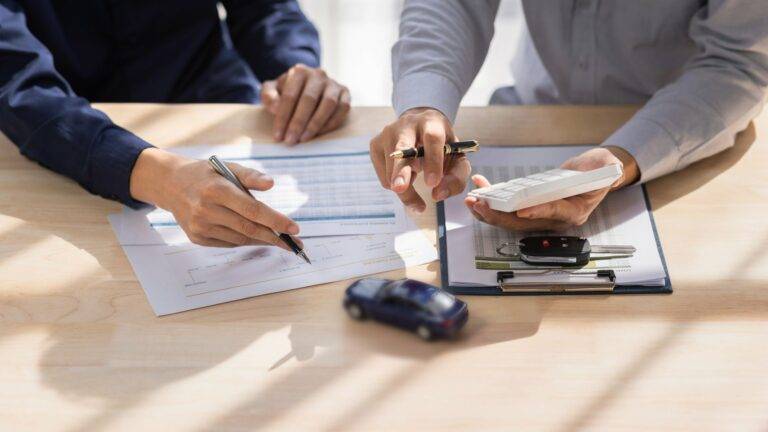 Two people calculating car loan payments with documents, a calculator, a car key, and a small model car on the table.