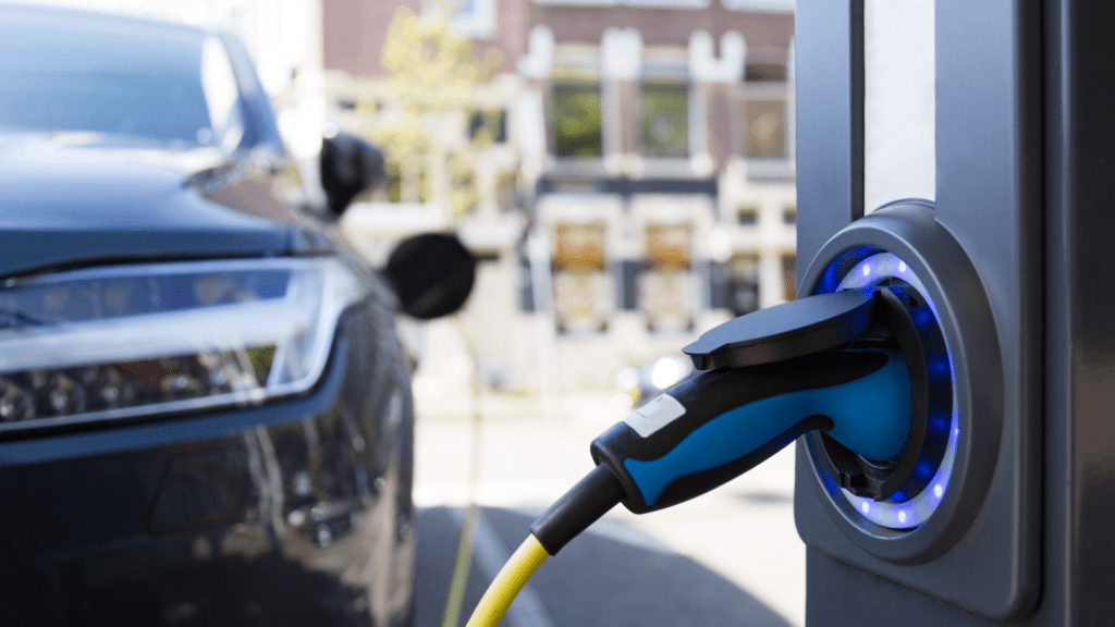 Electric vehicle charging at an outdoor station with a blue and yellow cable in an urban setting.