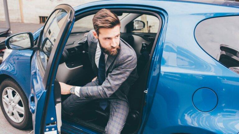 Man in a plaid suit stepping out of a blue car in an urban setting.