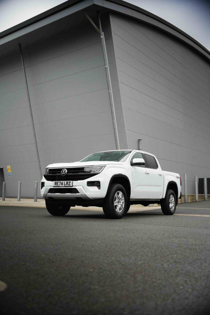 A white Volkswagen Amarok pickup truck parked in front of a modern gray building